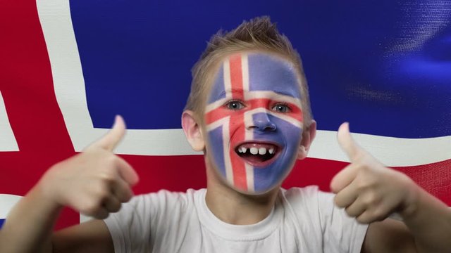 Joyful fan on the background of the flag of Iceland. Happy boy with painted face in national colors. The young fan rejoices in the victory of his beloved team. Success. Victory. Triumph.