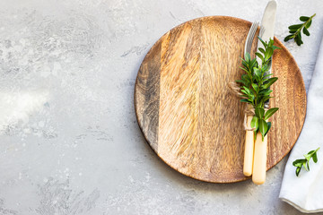 Empty wooden plate with fork, knife and boxwood on light grey stone background, top view. Mock up.