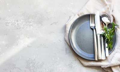 Elegant table setting with black ceramic plate, cutlery and canvas napkin on grey stone background. Space for text.