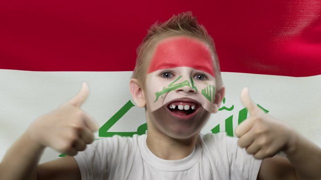 Joyful fan on the background of the flag of the Iraq. Happy boy with painted face in national colors. The young fan rejoices in the victory of his beloved team. Success. Victory. Triumph.
