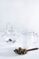 Obraz na płótnie Canvas Empty teapot and empty glass near wooden spoon filled blue thai tea