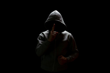 A man in a hood with a black face comes out of the darkness and asks to shut up by raising his...
