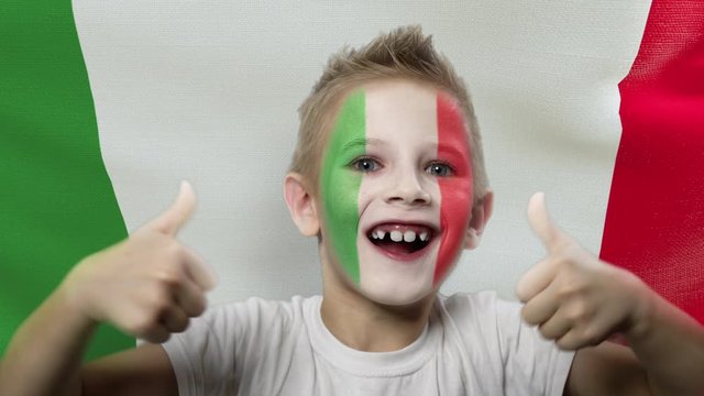 Joyful fan on the background of the flag of Italy. Happy boy with painted face in national colors. The young fan rejoices in the victory of his beloved team. Success. Victory. Triumph.