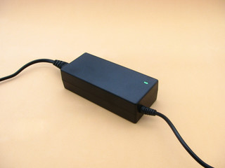 black battery charger for laptop. power supply for the battery. beige background. green light