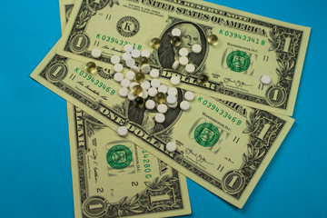 Scattered pills, drugs on three dollar bills on a blue background, pharmacist, expensive pills.