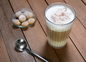 Glass latte macchiato with chocolate powder on foam and some cokkies  and spoon on wooden table
