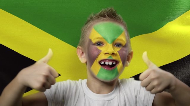 Joyful fan on the background of the flag of Jamaica. Happy boy with painted face in national colors. The young fan rejoices in the victory of his beloved team. Success. Victory. Triumph.