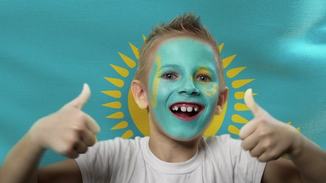 Joyful fan on the background of the flag of Kazakhstan. Happy boy with painted face in national colors. The young fan rejoices in the victory of his beloved team. Success. Victory. Triumph.