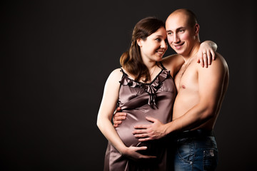 Photo of pregnant woman with brown hair and dressed hugging bald naked torso man