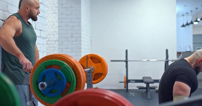 Heavyweight athlete lays down on a bench to pump arm muscles. Coach insures the heavyweight athlete. Gym.