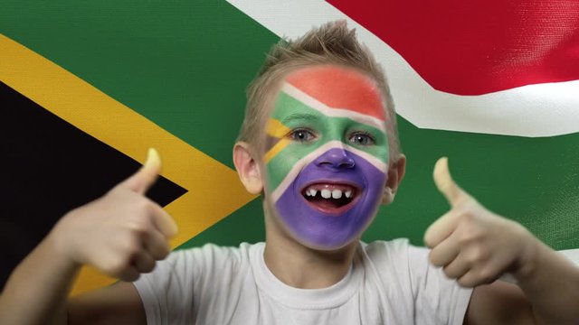 Joyful fan on the background of the flag of South Africa. Happy boy with painted face in national colors. The young fan rejoices in the victory of his beloved team. Success. Victory. Triumph.