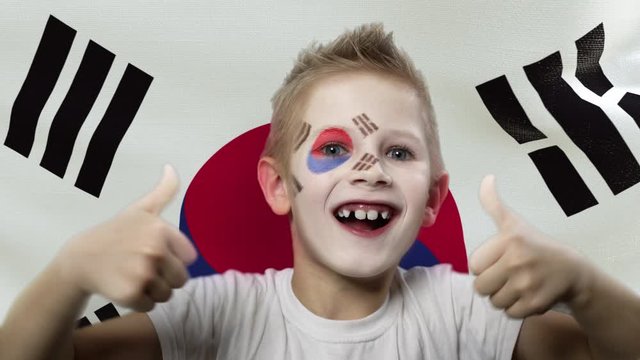 Joyful fan on the background of the flag of South Korea. Happy boy with painted face in national colors. The young fan rejoices in the victory of his beloved team. Success. Victory. Triumph.