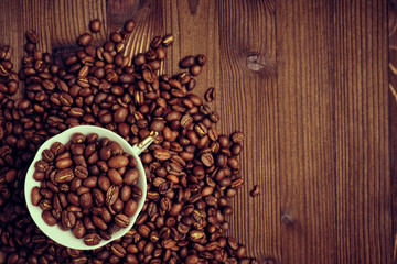 White cup on roasted coffee beans and a burnt wooden board. Copy space. Toned.