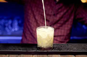 The bartender adds milk to a glass with ice while making an alcoholic drink.