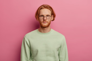 Young handsome man has red hair and beard, looks seriously at camera, listens necessary information...