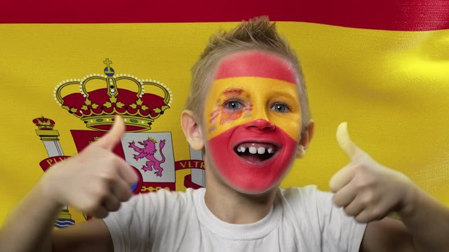 Joyful fan on the background of the flag of Spain. Happy boy with painted face in national colors. The young fan rejoices in the victory of his beloved team. Success. Victory. Triumph.