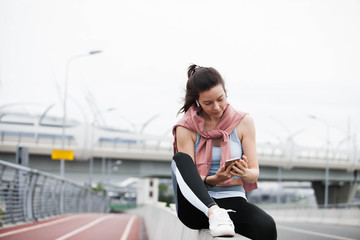 Athletic young woman in sports uniform installs music, checks the fitness application on smartphone, catches a network.