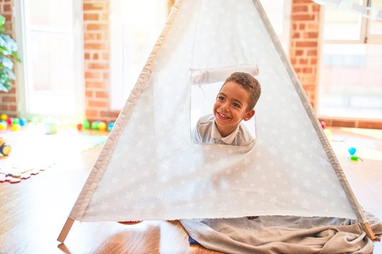 Beautiful african american toddler playing inside tipi smiling at kindergarten