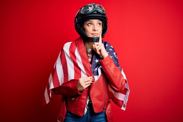 Young beautiful patriotic motorcyclist woman wearing motorcycle helmet and united states flag serious face thinking about question, very confused idea