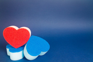 Obraz premium Red heart shape dishwash sponge over two blue heart shape dishwasher sponge in the foreground on the blue background