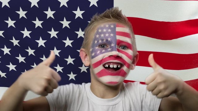 Joyful fan on the background of the flag of the USA. Happy boy with painted face in national colors. The young fan rejoices in the victory of his beloved team. Success. Victory. Triumph.