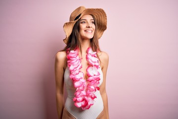 Young beautiful brunette woman on vacation wearing swimsuit and Hawaiian flowers lei looking away to side with smile on face, natural expression. Laughing confident.