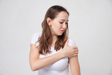 A girl in a white T-shirt massages her shoulder in pain.