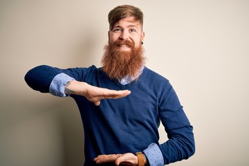 Handsome Irish redhead business man with beard standing over isolated background gesturing with hands showing big and large size sign, measure symbol. Smiling looking at the camera. Measuring concept.