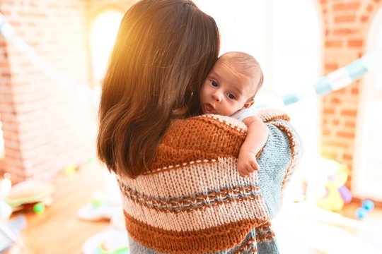 Young beautiful woman and her baby standing at home. Mother holding and hugging newborn