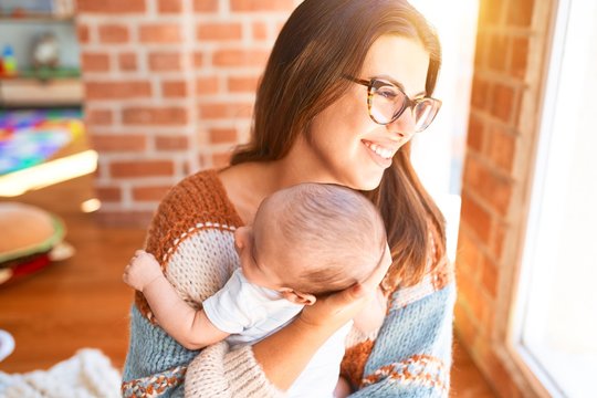 Young beautifull woman and her baby standing at home. Mother holding and hugging newborn