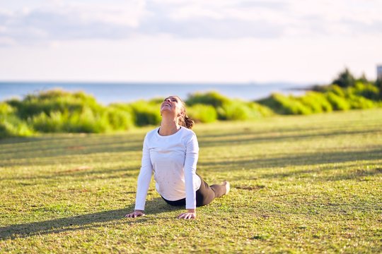 Young beautiful sportwoman practicing yoga. Coach teaching upward-facing dog pose at park