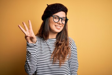 Young beautiful brunette woman wearing french beret and glasses over yellow background showing and...