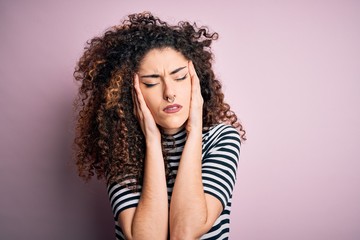 Young beautiful woman with curly hair and piercing wearing casual striped t-shirt with hand on head for pain in head because stress. Suffering migraine.