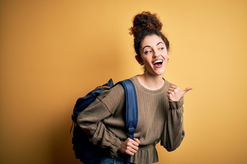 Young beautiful student woman with curly hair and piercing wearing backpack pointing and showing with thumb up to the side with happy face smiling