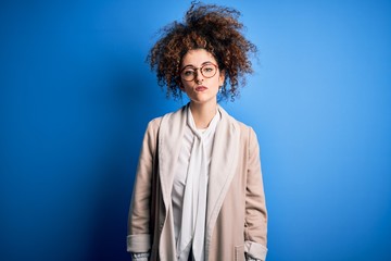 Young beautiful businesswoman with curly hair and piercing wearing jacket and glasses with serious expression on face. Simple and natural looking at the camera.