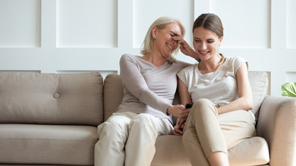 Smiling senior mom and daughter watch funny video on cell