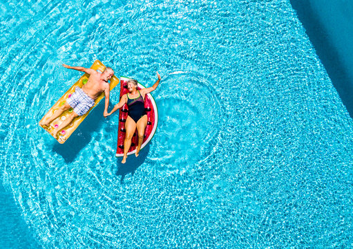 Vertical view of happy couple of old senior people enjoying the summer holiday vacation at the blue water pool with coloured treny lilos together with fun and love - Powered by Adobe