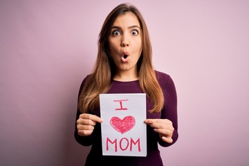 Young beautiful woman holding paper with love mom message celebrating mothers day scared in shock...