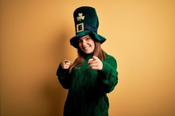 Young beautiful brunette woman wearing green hat on st patricks day celebration pointing fingers to camera with happy and funny face. Good energy and vibes.