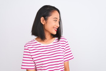 Fototapeta premium Young chinese woman wearing striped t-shirt standing over isolated white background looking away to side with smile on face, natural expression. Laughing confident.