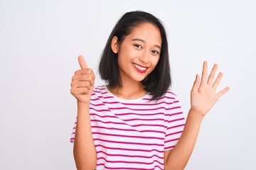 Young chinese woman wearing striped t-shirt standing over isolated white background showing and pointing up with fingers number six while smiling confident and happy.