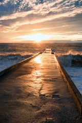 Big waves breaking on a stone pier in stormy weather with a bright sunset, a big tide. Black Sea. Sochi, February.