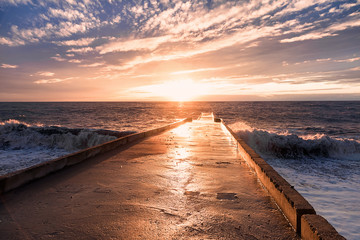 Big waves breaking on a stone pier in stormy weather with a bright sunset, a big tide. Black Sea. Sochi, February.