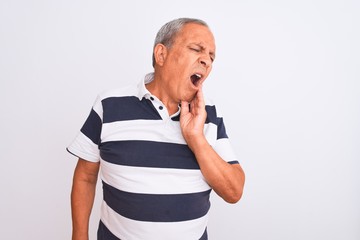Senior grey-haired man wearing casual striped polo standing over isolated white background touching mouth with hand with painful expression because of toothache or dental illness on teeth. Dentist