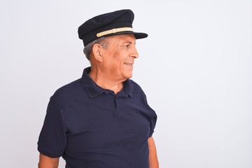 Senior grey-haired man wearing black polo and captain hat over isolated white background looking away to side with smile on face, natural expression. Laughing confident.