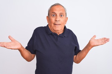 Fototapeta premium Senior grey-haired man wearing black casual polo standing over isolated white background clueless and confused expression with arms and hands raised. Doubt concept.