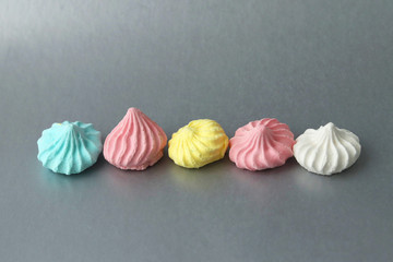 Colorful bright meringues in blue, pink and white in a row on a gray background. Fresh homemade treats. Selective focus.