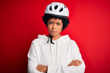 Young African American afro cyciling woman with curly hair wearing bike security helmet skeptic and nervous, disapproving expression on face with crossed arms. Negative person.