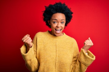 Fototapeta na wymiar Young beautiful African American afro woman with curly hair wearing casual yellow sweater celebrating surprised and amazed for success with arms raised and open eyes. Winner concept.