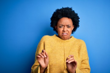 Young beautiful African American afro woman with curly hair wearing yellow casual sweater disgusted expression, displeased and fearful doing disgust face because aversion reaction. - obrazy, fototapety, plakaty